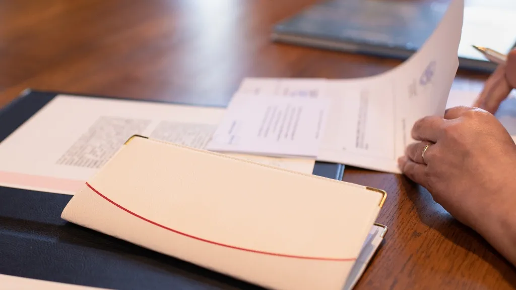 Person reviewing documents on a wooden table with a white folder and paperwork.