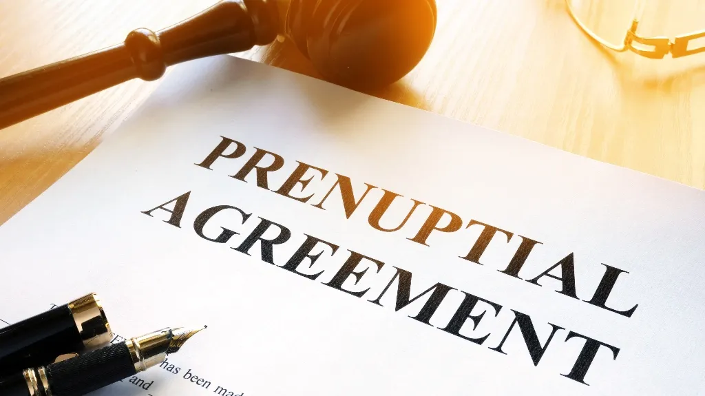 Close-up of a prenuptial agreement document with a fountain pen and wooden gavel on a light wooden surface.