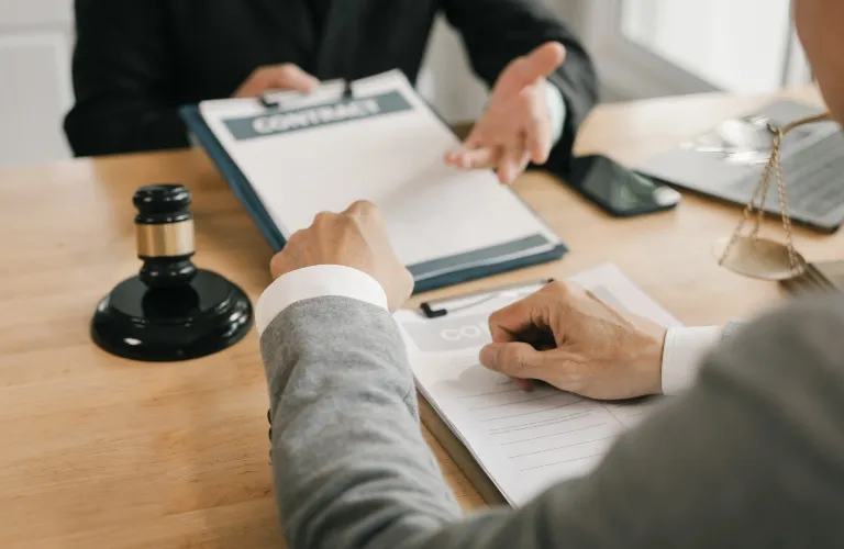 Two individuals in business attire reviewing contract documents at a wooden desk with a gavel and scales of justice.