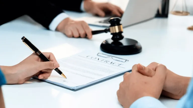 Person signing a contract document on a white table with a judge's gavel nearby.