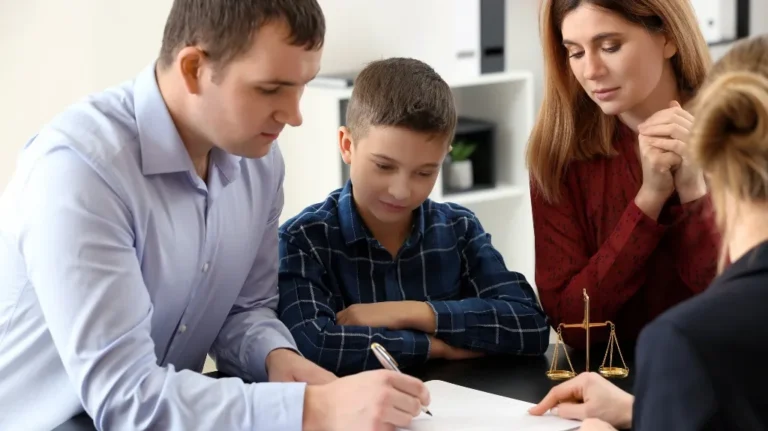 Four people, including a child, seated at a table with legal scales, signing a document.