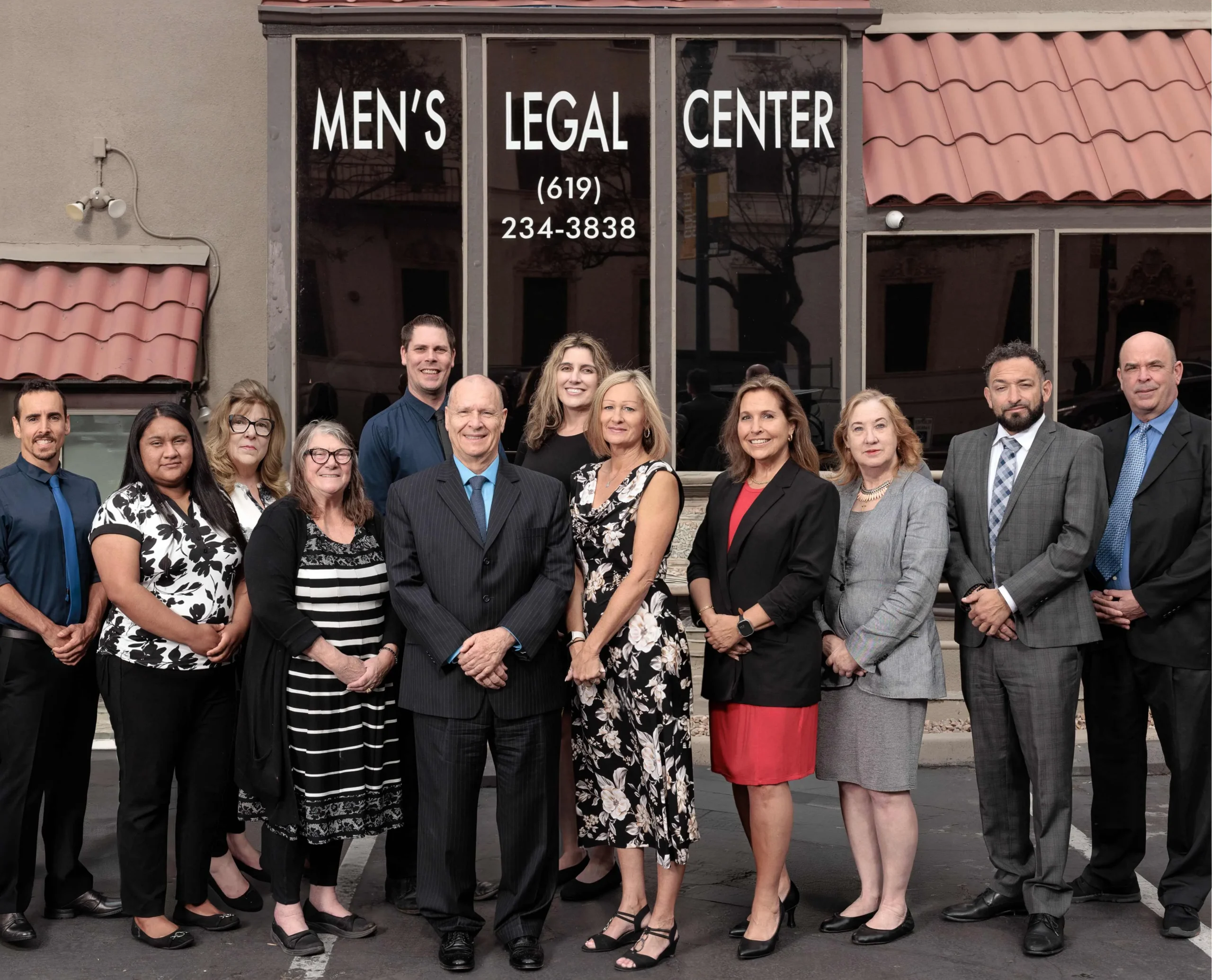 Group of professionally dressed men and women standing outside Men’s Legal Center with contact number visible.