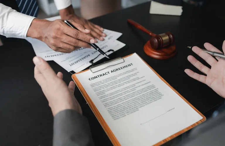 Two professionals reviewing a contract agreement on a clipboard with a wooden gavel nearby.
