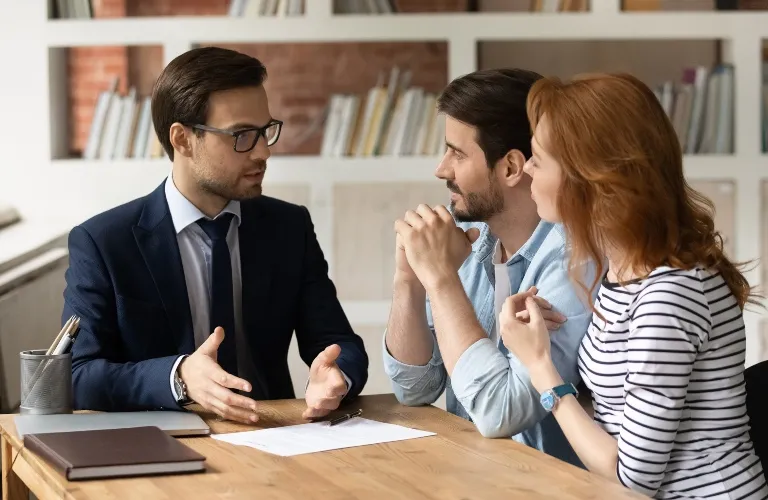 Three adults engaged in a business discussion at a wooden table with documents.