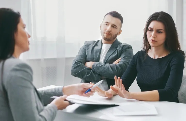 Three adults in a professional setting, woman in black refusing to sign a document.