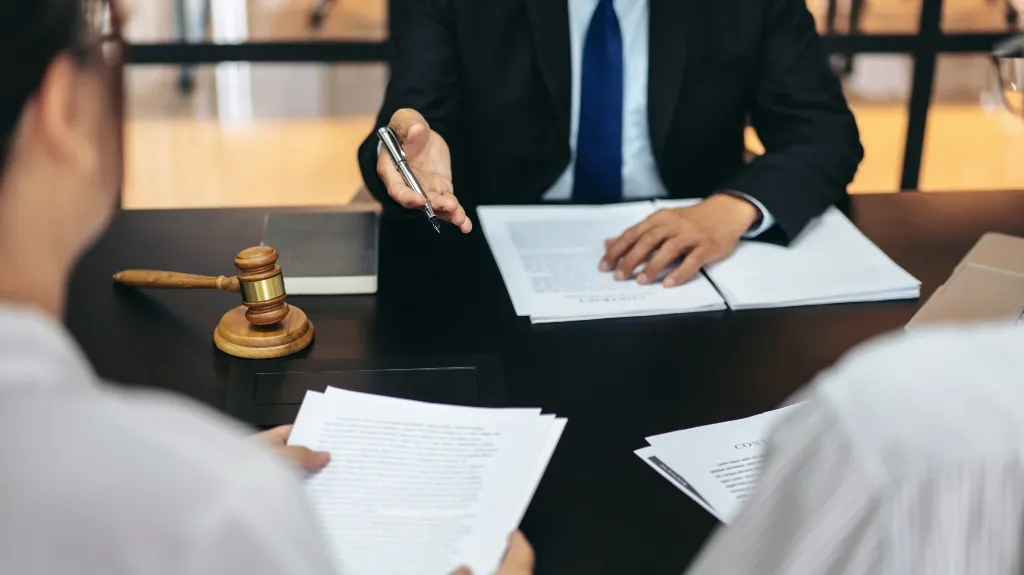 Two individuals reviewing legal documents with a lawyer in a suit at a black desk.
