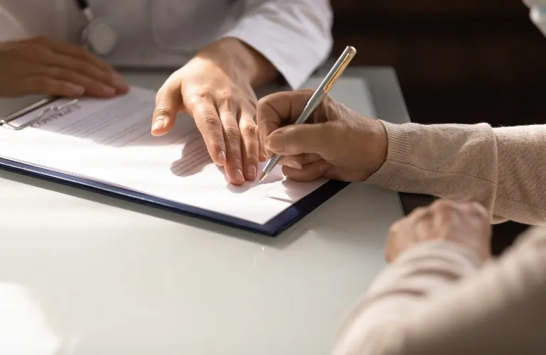 Two people at a desk, one signing a document while the other points on the paper.