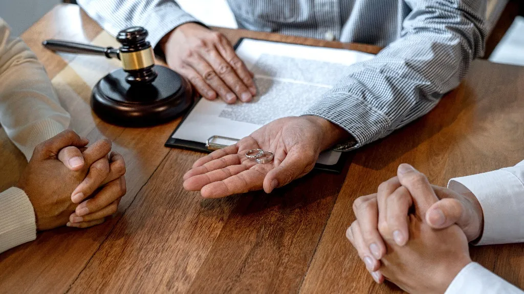 Legal professional holding wedding rings with gavel and document on wooden table.