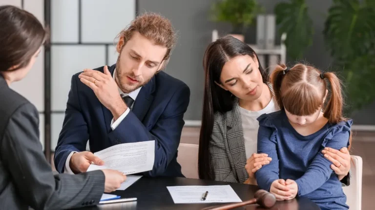 A man in a suit reviewing documents, a woman comforting a young girl at a table with legal papers.