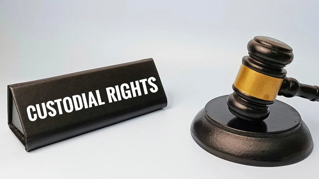 Black leather nameplate with "CUSTODIAL RIGHTS" text beside a wooden judge's gavel on white background.
