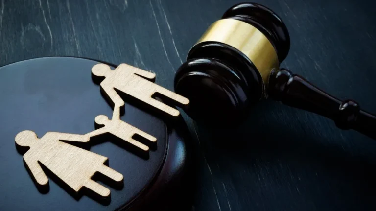 Wooden family figure with two adults and a child next to a judge's gavel on a dark surface.