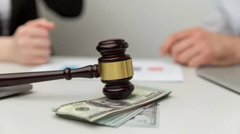 Wooden judge gavel resting on a stack of US dollar bills with blurred hands in background.