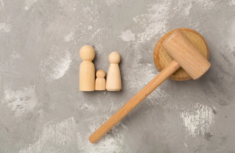 Wooden figurines representing a family beside a wooden gavel on a gray textured surface.