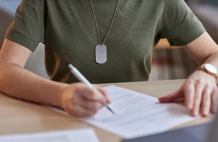 Person wearing an olive green shirt and dog tag necklace, signing a document.
