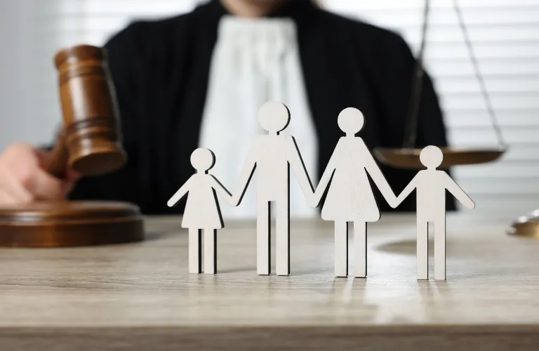 Wooden family figures on table with judge holding gavel and scales of justice background.