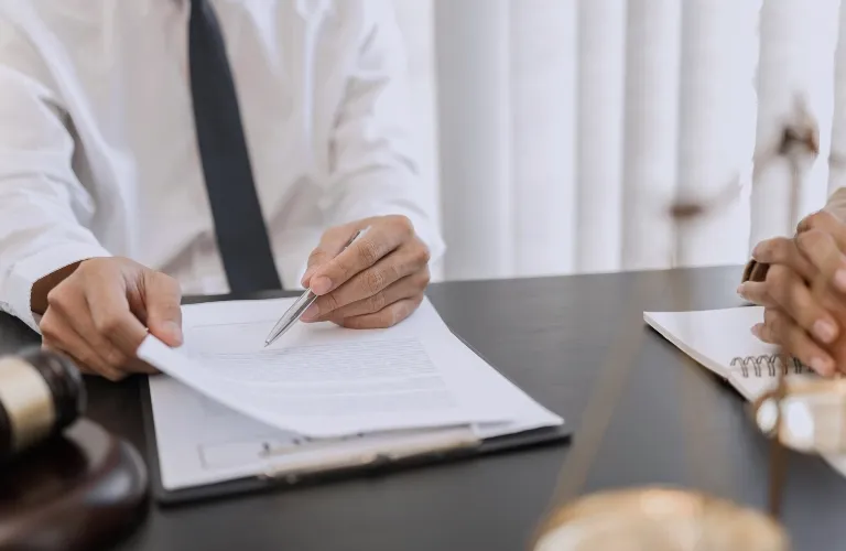 Two individuals in formal attire reviewing legal documents at a desk with a gavel and scales of justice.