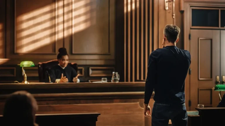 Man standing in a courtroom facing a female judge seated behind a wooden bench.