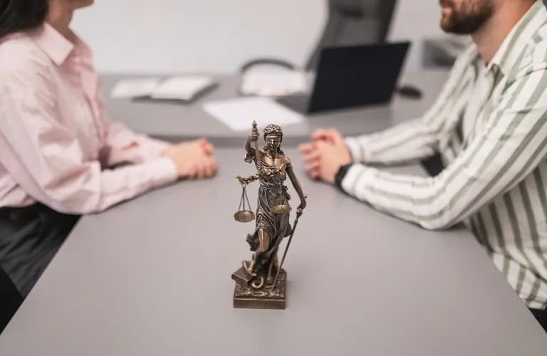 Bronze Lady Justice statue centered on a gray table between two seated individuals in a professional setting.
