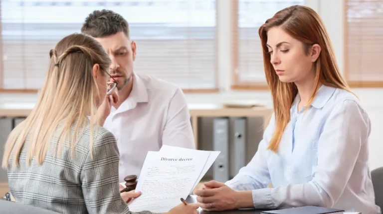 Three individuals, two women and one man, seated at a table reviewing a divorce decree document.