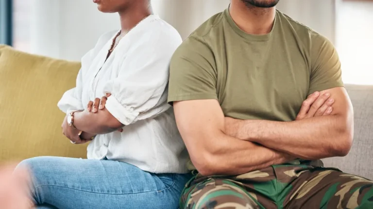 Two individuals sitting back-to-back on a couch with arms crossed, appearing upset.