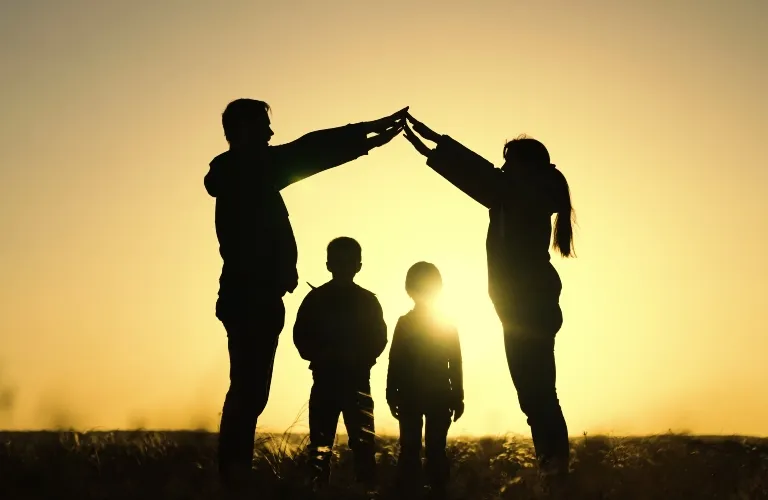 Silhouetted family of four at sunset, two adults forming a roof shape with their hands.