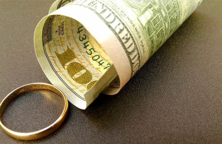 Close-up of a rolled one hundred dollar bill and a gold ring on a dark surface.