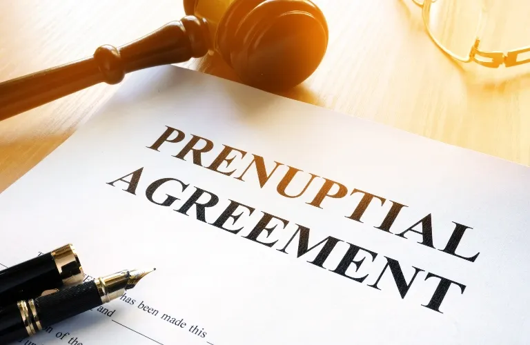 Close-up of a prenuptial agreement document with a pen and wooden gavel on a wooden surface.