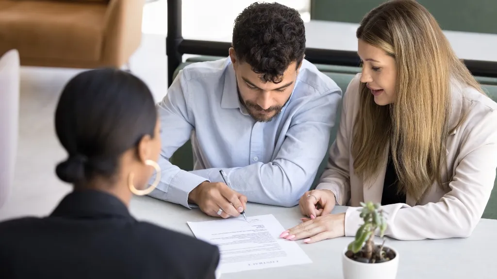 Three professionals, two women and one man, reviewing and signing a document at a table.