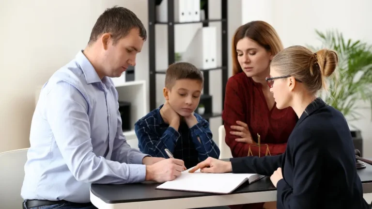 Professional woman in glasses explaining documents to a man, woman, and child at a table.