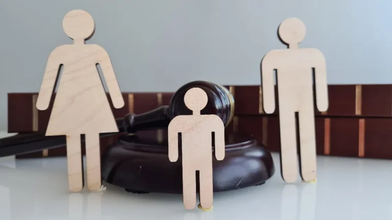 Wooden figurines of a woman, man, and child with a judge's gavel and law books in the background.